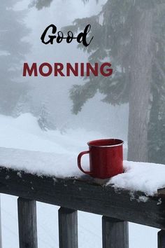 a red coffee cup sitting on top of a wooden railing next to snow covered trees