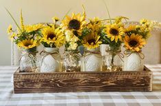 sunflowers and mason jars are arranged in a wooden tray on a checkered tablecloth