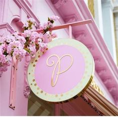 a pink and gold sign hanging from the side of a building with flowers in front of it