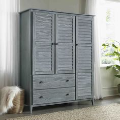 a gray armoire in front of a window with a rug and potted plant