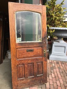 an old wooden door is open on the brick walkway outside a house with potted trees in the background