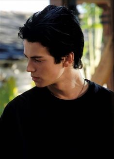 a young man with black hair is looking down at his cell phone while wearing a black t - shirt