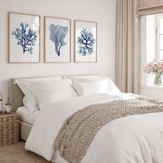 a bed with white linens and blue seaweed prints on the wall above it