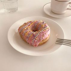 a donut with pink icing and sprinkles sits on a plate