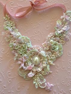 a pink and green necklace with flowers on it's sides, attached to a pink ribbon