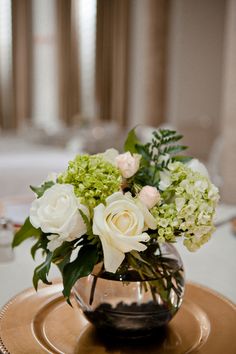 a vase filled with white and green flowers on top of a gold plated table