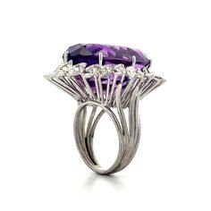 This vibrant cocktail ring features a 27.97-carat oval cut amethyst, radiating a rich purple hue. Surrounding the amethyst is a halo of twenty-four (24) single cut diamonds, each weighing .03 carats, creating a sparkling frame that enhances the beauty of the center stone. Crafted in polished 14 karat white gold, this ring offers a sleek setting that showcases the vibrant colors and sparkling accents. Ideal for both special events and adding flair to an everyday look, this cocktail ring is bold and striking. Luxury Purple Rings For Party, Luxury Purple Party Rings, Purple Oval Rings For Party, Purple Oval Party Rings, Engagement Ring Style Guide, Ring Style Guide, Platinum Rose Gold, Diamond Cocktail Ring, Sapphire Solitaire