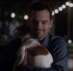 a man holding a dog in his arms at night with christmas lights on the background