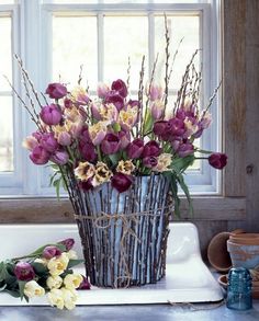 purple and yellow flowers in a blue vase on a white tray next to a window