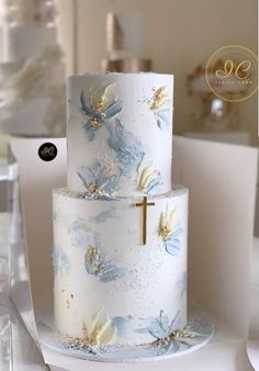 a three tiered cake with blue flowers and a cross on the top is sitting on a table