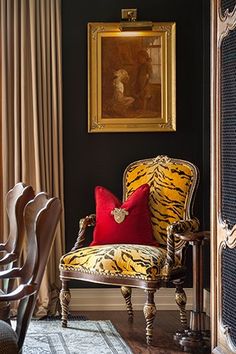 a tiger print chair with red pillows in front of a painting on the black wall