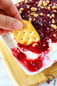 a person dipping crackers into a berry dessert