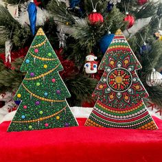 two christmas trees sitting on top of a red blanket next to a tree with ornaments