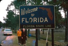 two women standing in front of a welcome to florida sign with a car behind them