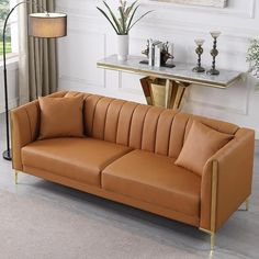 a tan leather couch sitting in front of a table with a lamp on top of it