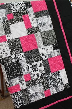 a black and white quilt with pink squares on the bottom is sitting on a chair