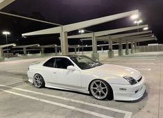 a white car is parked in an empty parking lot at night with its lights on