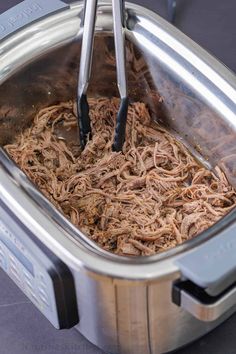 a slow cooker filled with meat and two tongs sticking out of the top