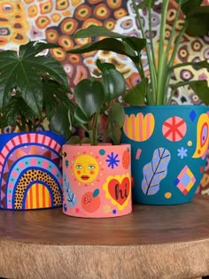 three potted plants sitting on top of a wooden table next to a colorful wall