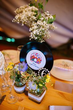 there is a table with flowers and records on it, as well as wine glasses