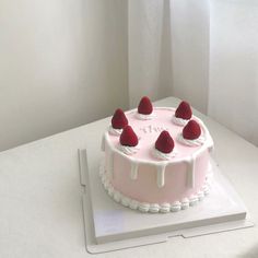 a pink cake with white icing and strawberries on top sitting on a table