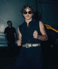 a man in black shirt and sunglasses standing next to another man with an electric guitar