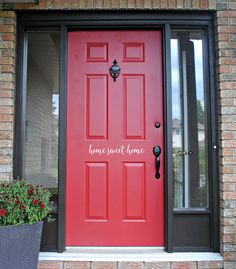 a red front door with the words home sweet home on it and potted plants