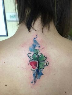 the back of a woman's neck is covered with watercolor tattoos and clovers