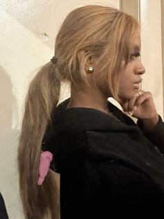 a woman with long hair standing in front of a mirror wearing a ponytail and looking into the distance