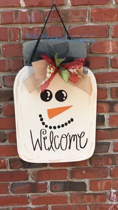 a snowman welcome sign hanging on the side of a brick wall with a bow