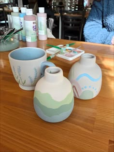 three vases sitting on top of a wooden table next to a bowl and cup