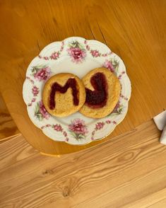 two cookies on a plate with the word m spelled out in front of them, sitting on a wooden table