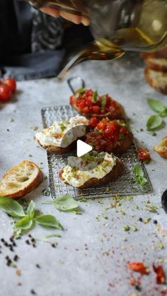 a person pouring wine into a glass next to bread and tomatoes on a table with other food items