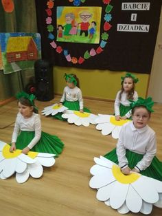 children in green and white dresses sitting on the floor with large paper flowers around them