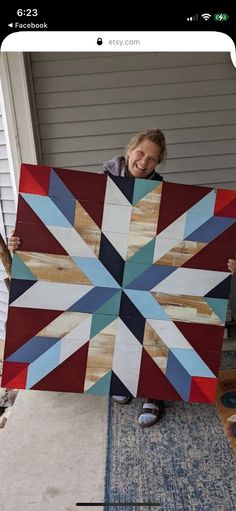 a woman holding up a large quilt made out of wood planks and scrapbook paper