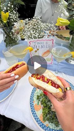 people sitting at a table eating hotdogs with condiments and flowers in the background