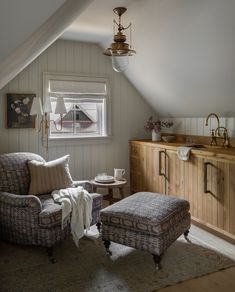 a chair and ottoman in a room with white walls, wooden floors and an atticed ceiling