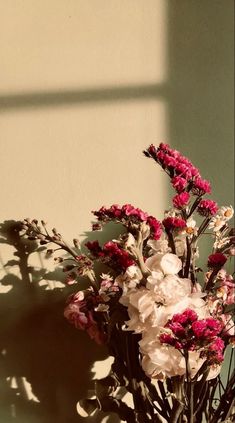 a vase filled with pink and white flowers on top of a wooden table next to a wall