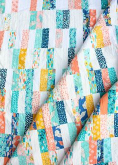 an orange, blue and white quilt on top of a bed sheet with multicolored squares