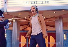 a man with headphones on standing in front of a movie theater and singing into a microphone