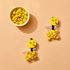 three yellow candies with faces on them in plastic bags next to a bowl of lemons