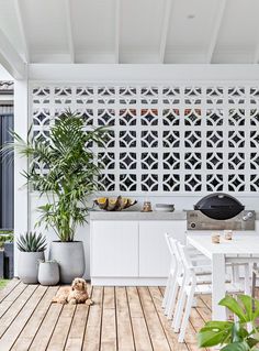 an outdoor kitchen and dining area with white table, chairs and potted plants on the deck