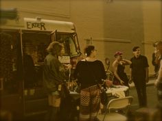 a group of people standing in front of a food truck talking to each other on the street