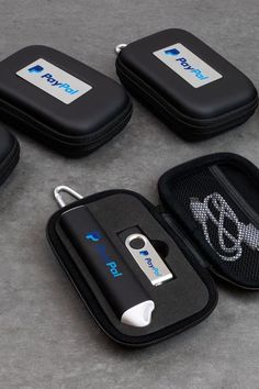 four cell phones in cases sitting on the ground with their tags attached to them, and one is plugged into an external charger