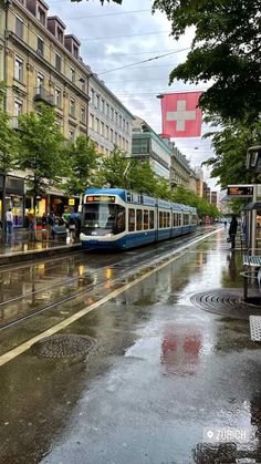 a blue and white train traveling down tracks next to tall buildings on a rainy day