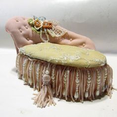 a doll laying on top of a pink couch covered in pearls and lace with a flower pinned to it's back