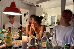 a group of people sitting around a table with food and drinks on it, in the kitchen