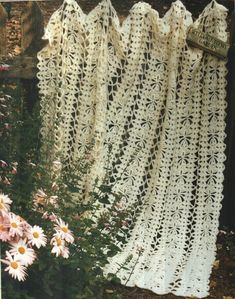 white crocheted curtains hanging from a wooden fence with daisies in the foreground