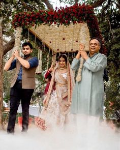 two men and a woman standing in front of a gazebo with flowers on it