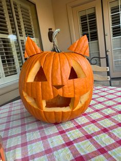 a pumpkin carved to look like a cat sitting on top of a checkered table cloth